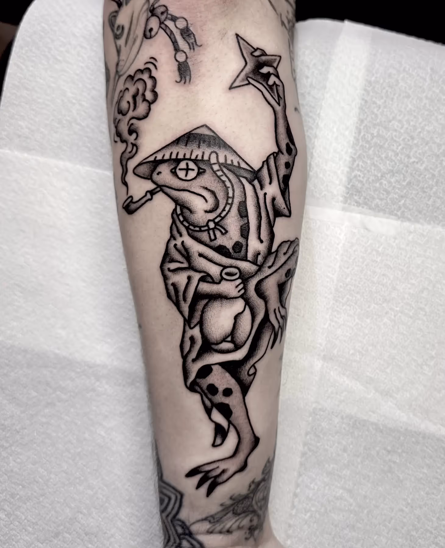 Blackwork tattoo van een Japanse kikker met hoed op onderarm, gezet door Nik Mart bij True Spirit Tattoo Barendrecht
