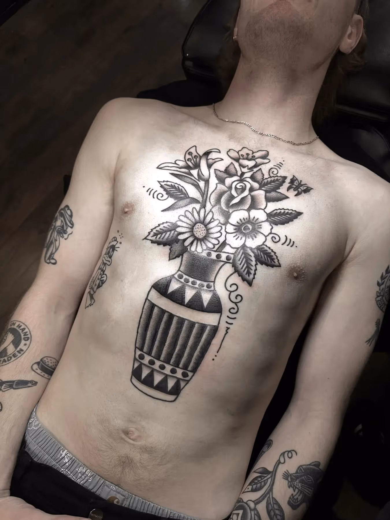 Blackwork tattoo van een vaas met bloemen op de borst, gezet door Nik Mart bij True Spirit Tattoo Barendrecht