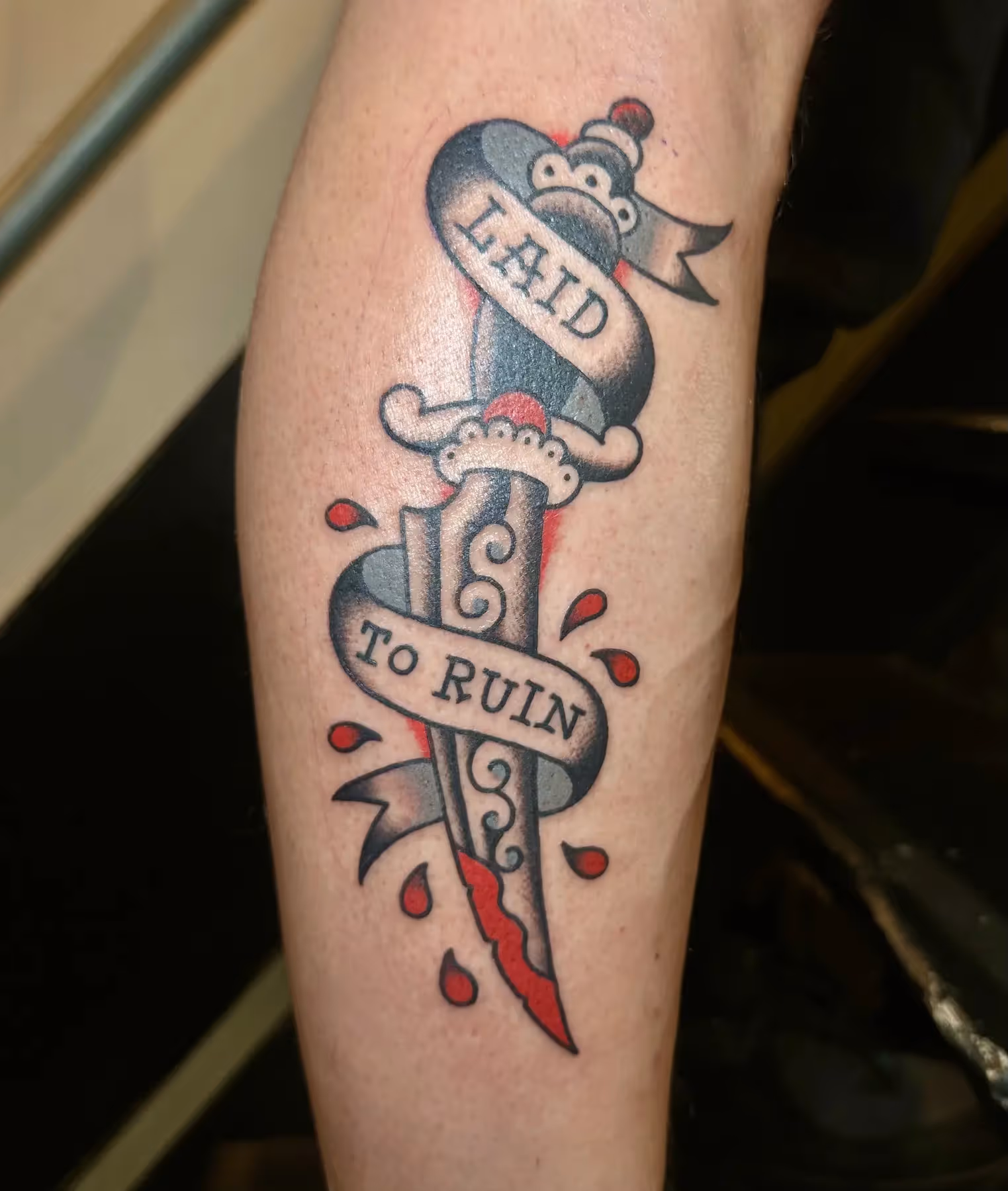Traditional dolk tattoo met banner op onderbeen, gezet door Nik Mart bij True Spirit Tattoo Barendrecht